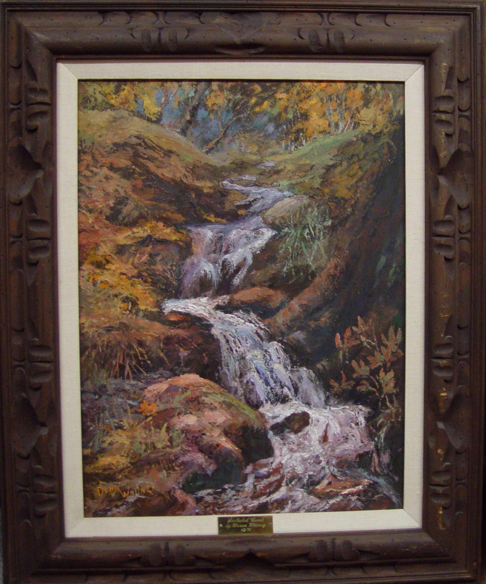"Secluded Creek" by Dona Whitney. Oil painting depicting a small stream flowing down hill over rocky ground. Surrounding growth painted in fall colors. 