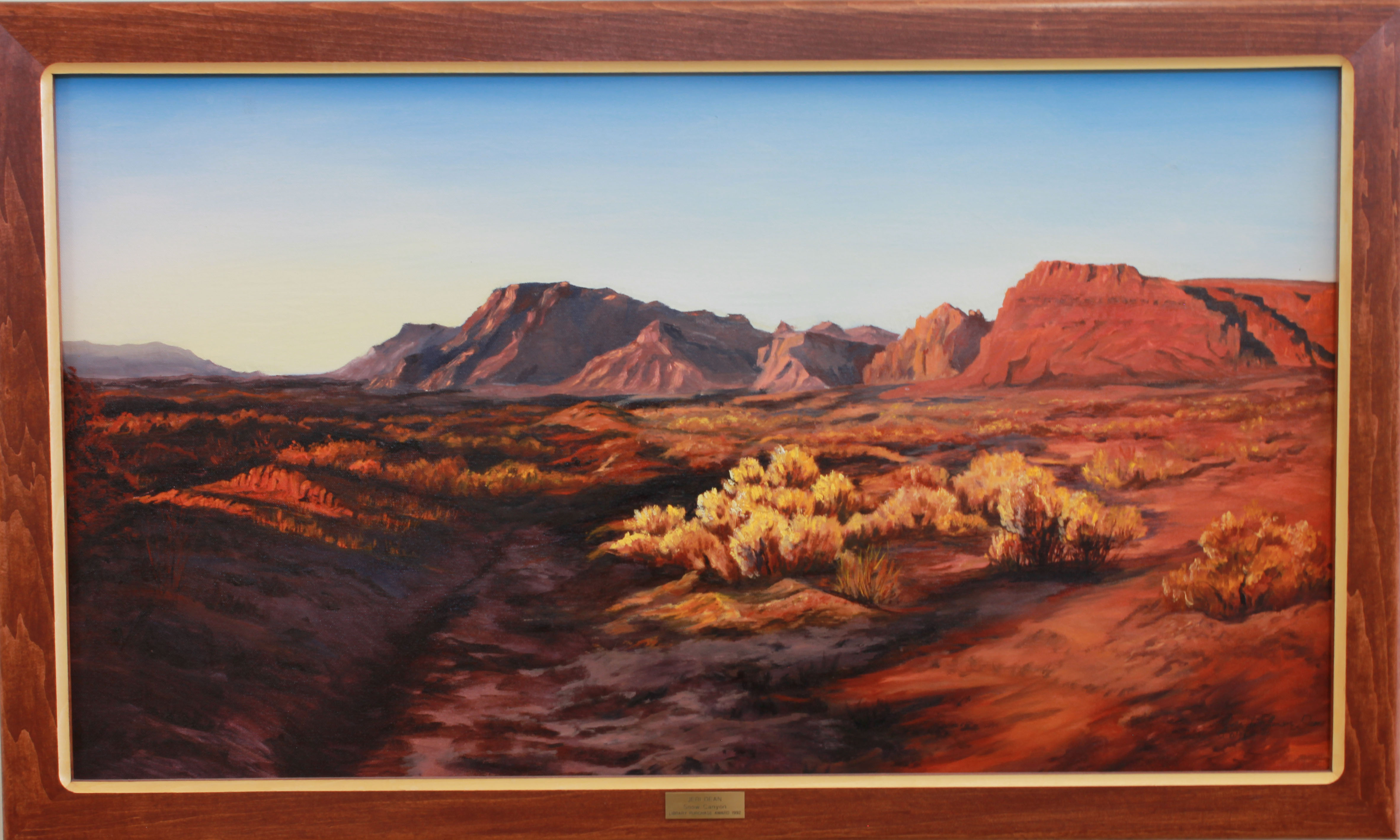 "Snow Canyon" by Jeri Dean. Oil painting of Snow Canyon. A desert landscape with red rock mountains in the distance. Yellow shrubbery in the foreground. Cloudless sky. 